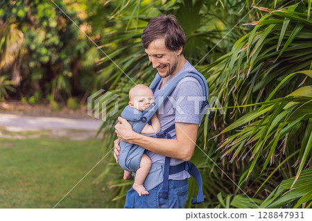 Young father walks in nature with his baby son nestled close in a parent-facing ergonomic baby carrier. Bonding, warmth, and modern parenting concept in a peaceful outdoor setting Young father walks in nature with his baby son nestled close in a parent-facing ergonomic baby carrier. Bonding, warmth, and modern parenting concept in a peaceful outdoor setting 128847931