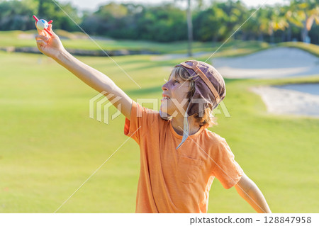 Boy wearing a pilot hat running through the grass with a toy airplane, dreaming of adventures. Childhood, imagination, and freedom concept Boy wearing a pilot hat running through the grass with a toy airplane, dreaming of adventures. Childhood, imagination, and freedom concept 128847958