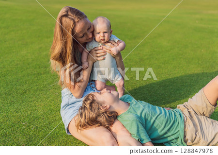 Mother, older son, and newborn baby on a meadow in the park. Family spending quality time together in nature. Parenthood, love, and family bond concept 128847978