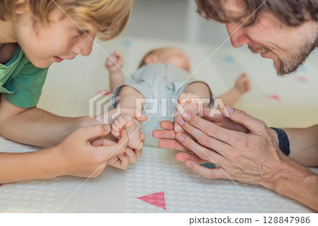 Father, son, and newborn baby lying on the floor in a cozy nursery, celebrating the arrival of their newest family member. Parenthood, bonding, and family love concept Father, son, and newborn baby lying on the floor in a cozy nursery, celebrating the arrival of their newest family member. Parenthood, bonding, and family love concept 128847986