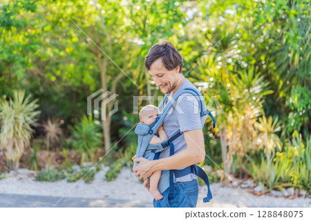 Young father walks in nature with his baby son nestled close in a parent-facing ergonomic baby carrier. Bonding, warmth, and modern parenting concept in a peaceful outdoor setting Young father walks in nature with his baby son nestled close in a parent-facing ergonomic baby carrier. Bonding, warmth, and modern parenting concept in a peaceful outdoor setting 128848075