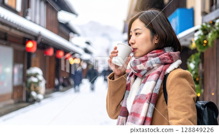 AI Image: A young woman wearing a coat drinking a hot drink in a snowy downtown area 128849226