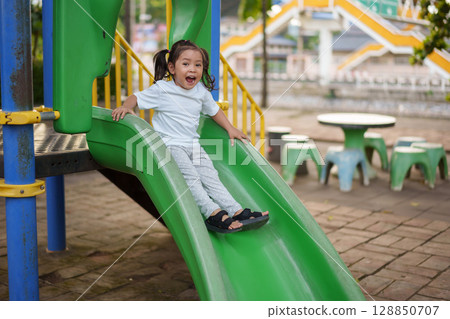 happy toddler baby girl sliding and playing at playground 128850707