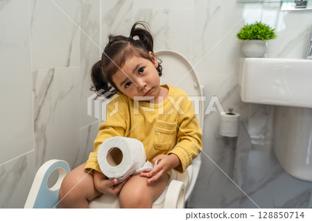 toddler girl sitting on toilet with tissue at home and suffering from stomachache and constipation 128850714