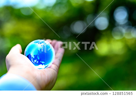 A crystal globe held up against beautiful new greenery - Ecology image - Dark blue 128851565