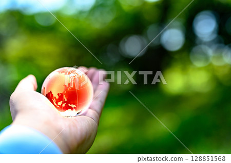 A crystal globe held up over beautiful new greenery - Ecology image - Global warming image 128851568