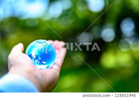 A crystal globe held up against beautiful new greenery - Ecology image - Blue normal 128851948
