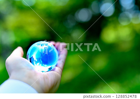 A crystal globe held up against beautiful fresh greenery - Ecology image - Blue 128852478