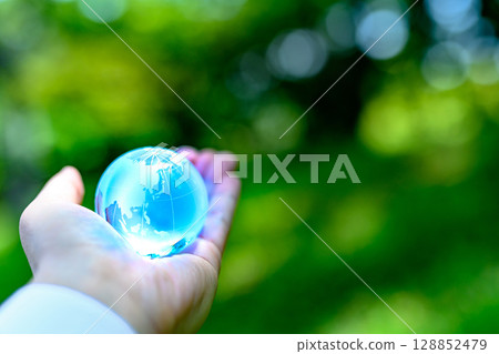 A crystal globe held up against beautiful new greenery. Ecological image. Light blue. 128852479