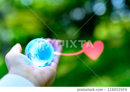 A crystal globe held over beautiful fresh greenery. Hearts gathering from the Earth. Ecology image. Light blue. A crystal globe held over beautiful fresh greenery. Hearts gathering from the Earth. Ecology image. Light blue. 128852959