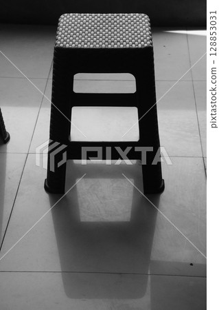 Black Plastic Stool on Tiled Floor with Dramatic Shadow 128853031