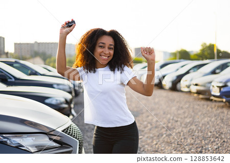 A happy woman shows off her new car keys after buying a vehicle at a dealership. 128853642