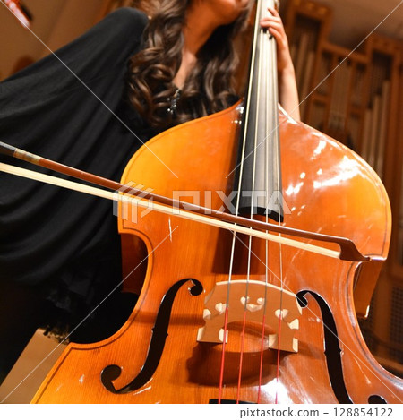 A female player playing the double bass at a recital A female player playing the double bass at a recital 128854122