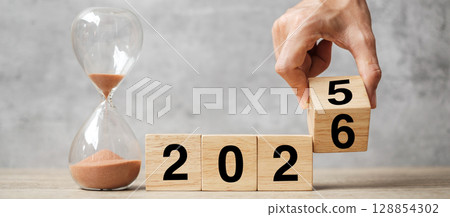 hand flipping block 2025 to 2026 text with hourglass on table. Resolution, time, plan, goal, motivation, reboot, countdown  and New Year holiday concepts 128854302