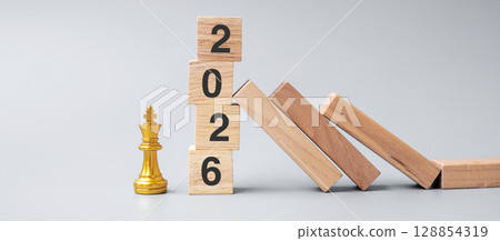 wooden Dominoes falling against 2026 stop blocks with golden Chess King figure. Business, Risk Management, Solution, economic, Insurance and New Year concept 128854319
