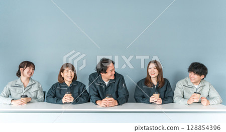 A woman and a man in work clothes drinking coffee in the office rest area 128854396
