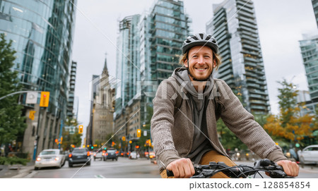 Smiling young man riding bicycle in modern city with glass buildings and traffic around. Urban lifestyle and eco transport concept. 128854854