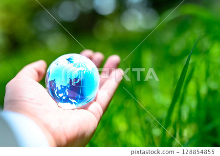 A crystal globe held up against beautiful fresh greenery - Ecology image - Blue 128854855