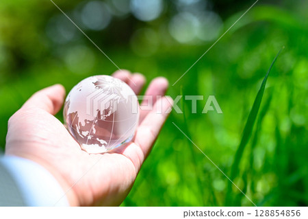 A crystal globe held up over beautiful new greenery - Ecology image - Normal color A crystal globe held up over beautiful new greenery - Ecology image - Normal color 128854856
