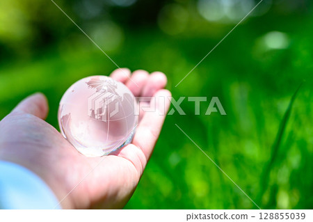A crystal globe held up over beautiful new greenery - Ecology image - Normal color 128855039