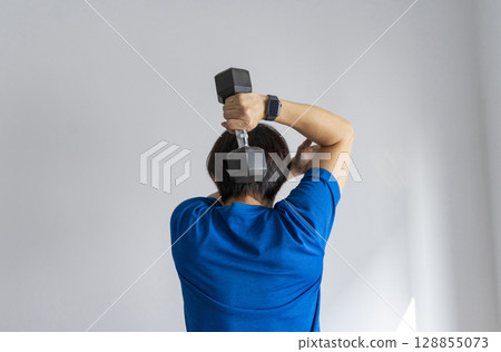 handsome man doing dumbbell workout at home, working on arms strength at living room interior. 128855073