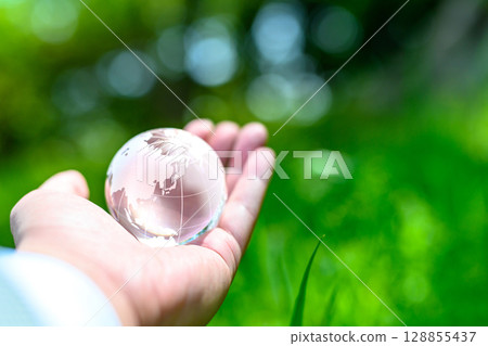 A crystal globe held up over beautiful new greenery - Ecology image - Normal color 128855437