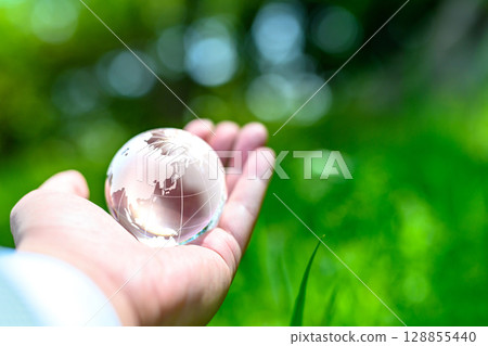 A crystal globe held up against beautiful new greenery. Ecological image. Clear normal color. 128855440