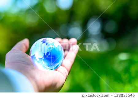A crystal globe held up against beautiful fresh greenery - Ecology image - Blue 128855546