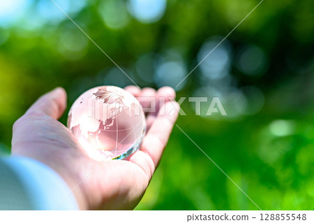 A crystal globe held up against beautiful new greenery. Ecological image. Clear normal color. 128855548