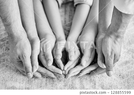 Top view of parents and kids holding empty hands together. Supportive family holding each others hands on background of white carpet. Concepts of teamwork, unity. Black and white image. Top view of parents and kids holding empty hands together. Supportive family holding each others hands on background of white carpet. Concepts of teamwork, unity. Black and white image. 128855599
