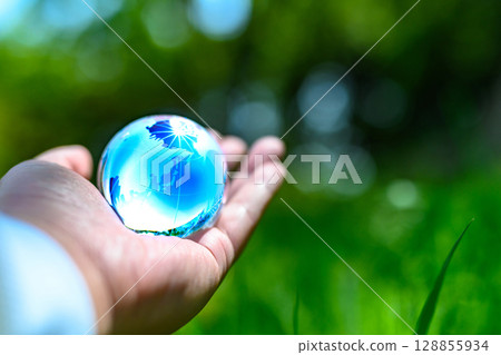 A crystal globe held up against beautiful fresh greenery - Ecology image - Blue A crystal globe held up against beautiful fresh greenery - Ecology image - Blue 128855934