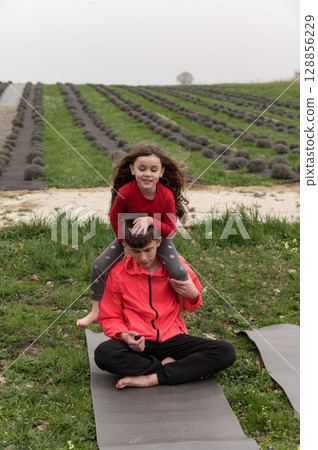 Joyful moments shared between a child and adult during an outdoor yoga session on a serene grassy field in early spring surrounded by rows of lavender 128856229