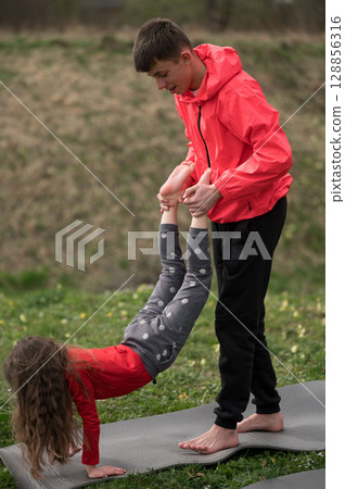 Joyful afternoon of yoga practice between siblings in a sunny park, showcasing teamwork and balance while embracing natures beauty 128856316