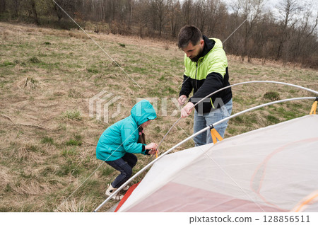 Father and daughter bonding while setting up a tent in the peaceful countryside during a sunny afternoon adventure 128856511