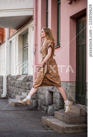 Young woman in linen dress jumping off urban stone stairs in city street 128856629