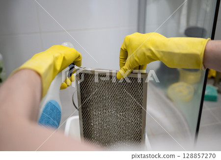 Cleaning dirty kitchen range hood grease filter with spray bottle and rubber gloves 128857270