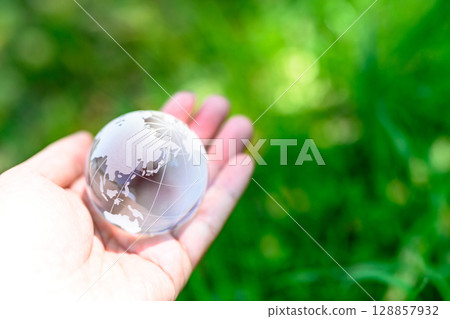 A crystal globe held over beautiful fresh greenery - an ecological image A crystal globe held over beautiful fresh greenery - an ecological image 128857932