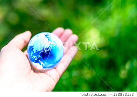 A crystal globe held over beautiful fresh greenery - Ecology image - A vivid blue color A crystal globe held over beautiful fresh greenery - Ecology image - A vivid blue color 128858158