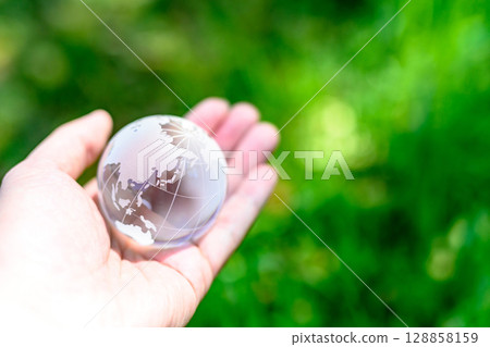 A crystal globe held over beautiful fresh greenery. Ecology image. Normal color. 128858159