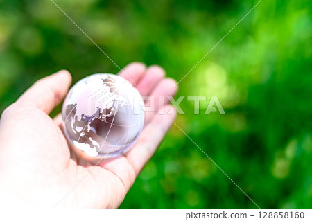 A crystal globe held over beautiful fresh greenery. Ecological image. Clear normal color. 128858160