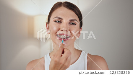 White female teenager with braces demonstrating dental care by using an oral irrigator. She smiles while holding irrigator near her braces, highlighting effective orthodontic hygiene practices. White female teenager with braces demonstrating dental care by using an oral irrigator. She smiles while holding irrigator near her braces, highlighting effective orthodontic hygiene practices. 128858256