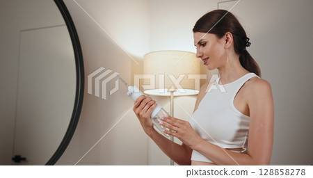 Young Caucasian woman with braces holding dental irrigator while smiling. Image depicts dental care and oral hygiene in home environment. Young Caucasian woman with braces holding dental irrigator while smiling. Image depicts dental care and oral hygiene in home environment. 128858278