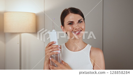Young Caucasian woman with braces using dental irrigator, promoting oral hygiene. She is smiling while demonstrating effective dental care tool, enhancing confidence and dental health. Young Caucasian woman with braces using dental irrigator, promoting oral hygiene. She is smiling while demonstrating effective dental care tool, enhancing confidence and dental health. 128858284