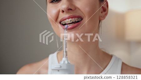 Young Caucasian woman with braces using dental irrigator, emphasizing oral hygiene, dental care, and smile enhancement. Young Caucasian woman with braces using dental irrigator, emphasizing oral hygiene, dental care, and smile enhancement. 128858321