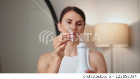 Young Caucasian woman with braces using dental irrigator. Focus on oral hygiene and dental care. Modern device ensures clean and healthy teeth in home setting, promoting confidence and well-being. 128858354