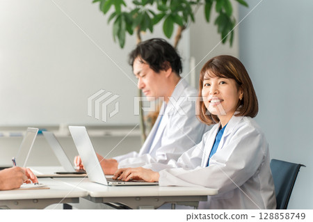 身穿白大褂的男女醫生坐在辦公桌前工作 128858749
