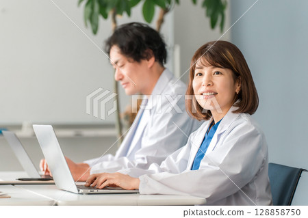 身穿白大褂的男女醫生坐在辦公桌前工作 128858750