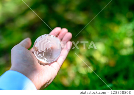 A crystal globe held over beautiful fresh greenery, an ecological image, a long shot 128858808
