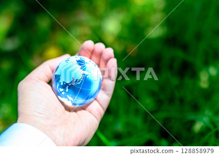 A crystal globe held over beautiful fresh greenery - Ecology image - Blue A crystal globe held over beautiful fresh greenery - Ecology image - Blue 128858979