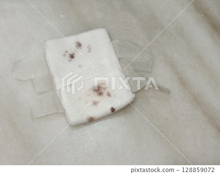 A used gauze pad with dried blood stain, placed on a table top.  128859072